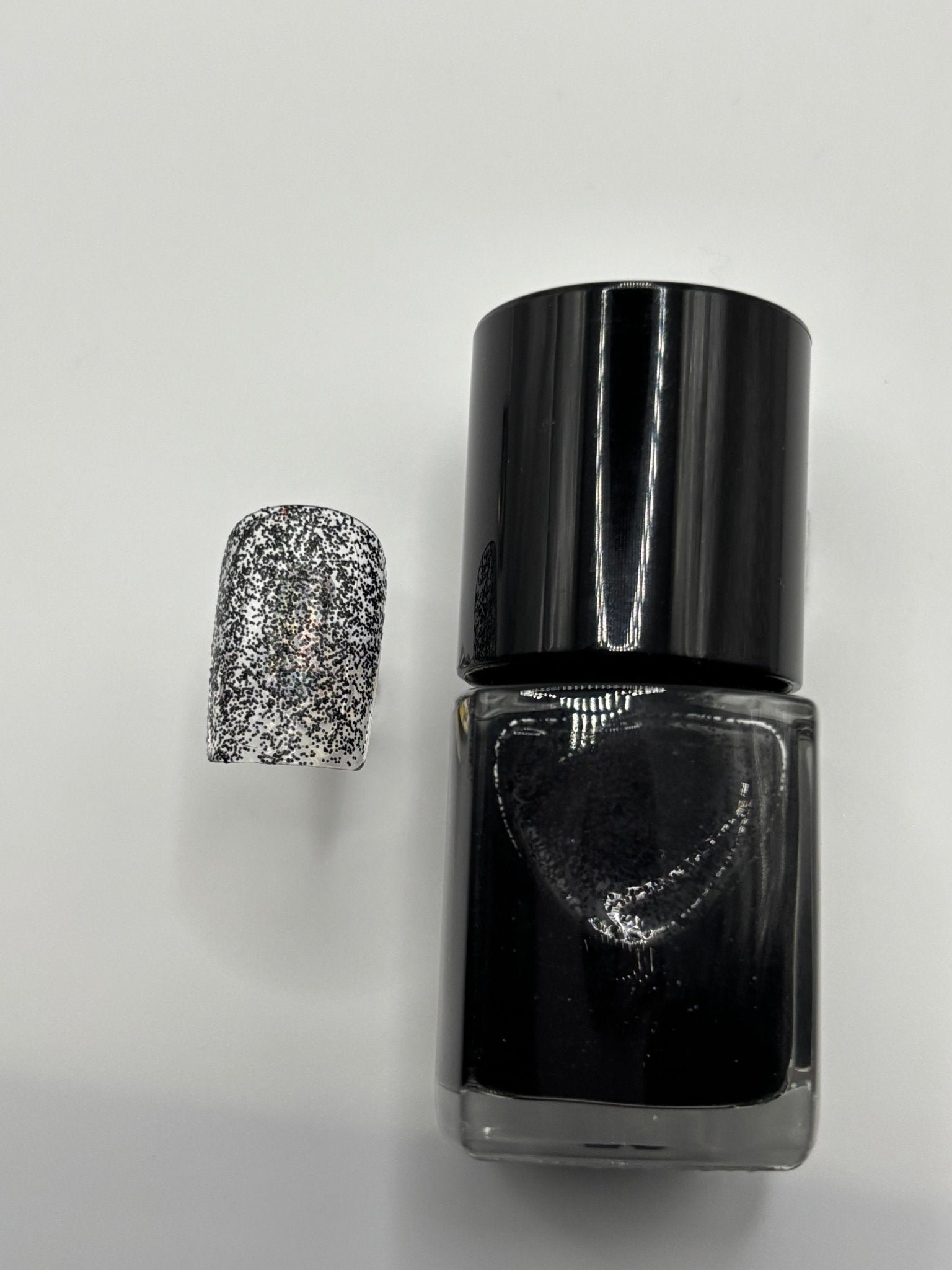 A BOTTLE OF MOLLY BLACK GLITTER POLISH WITH A FAKE FINGERNAIL WITH MOLLY ON IT