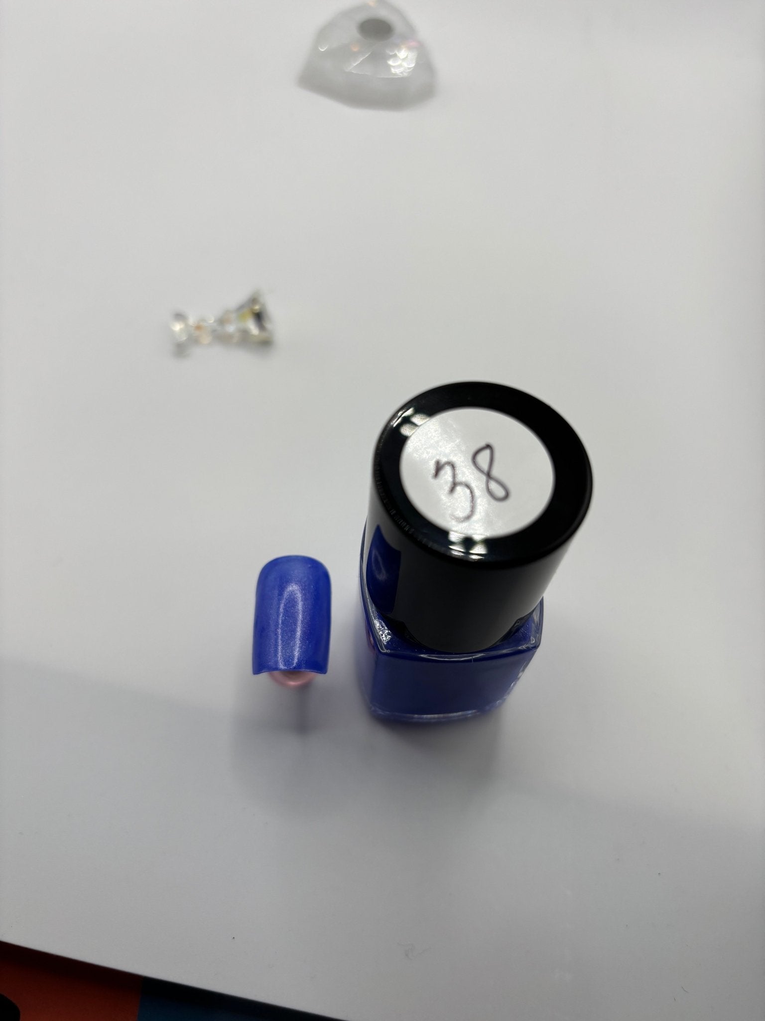 BOTTLE OF TIGE WITH A FAKE FINGERNAIL BESIDE IT THE SAME COLOR WITH THE NUMBER #37 ON THE TOP